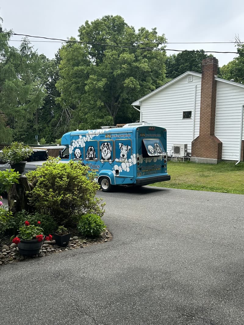 The blue Premier Paws grooming van parked on a customer's driveway beside a white house